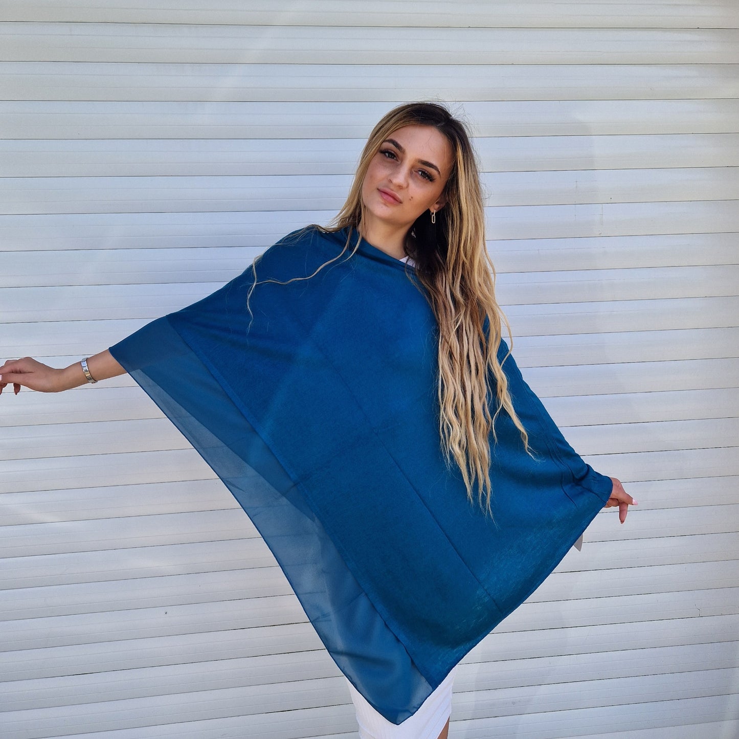 Young lady wearing a petrol blue coloured poncho with chiffon trim.