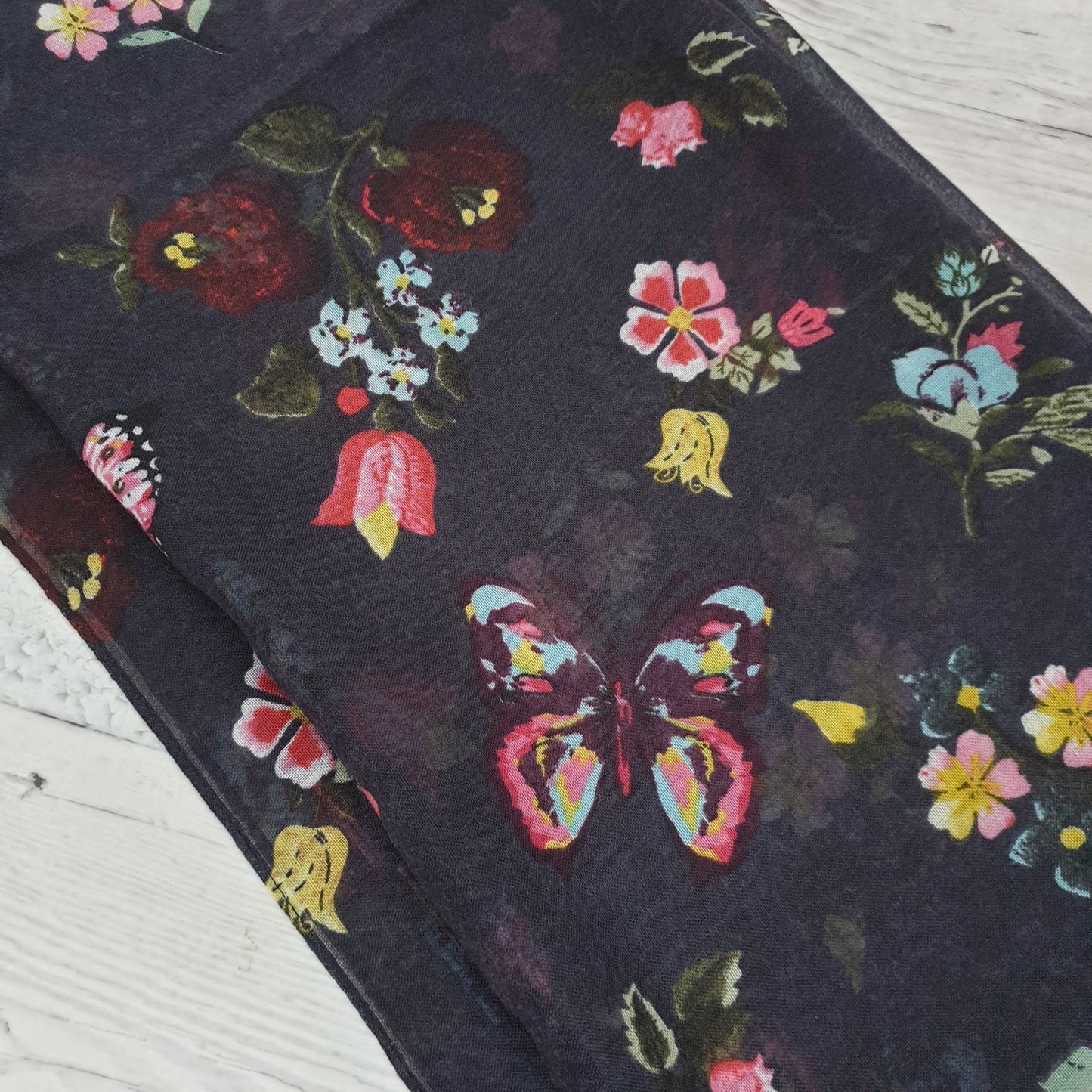 Photo of a black scarf decorated with yellow, pink and blue flowers and butterflies
