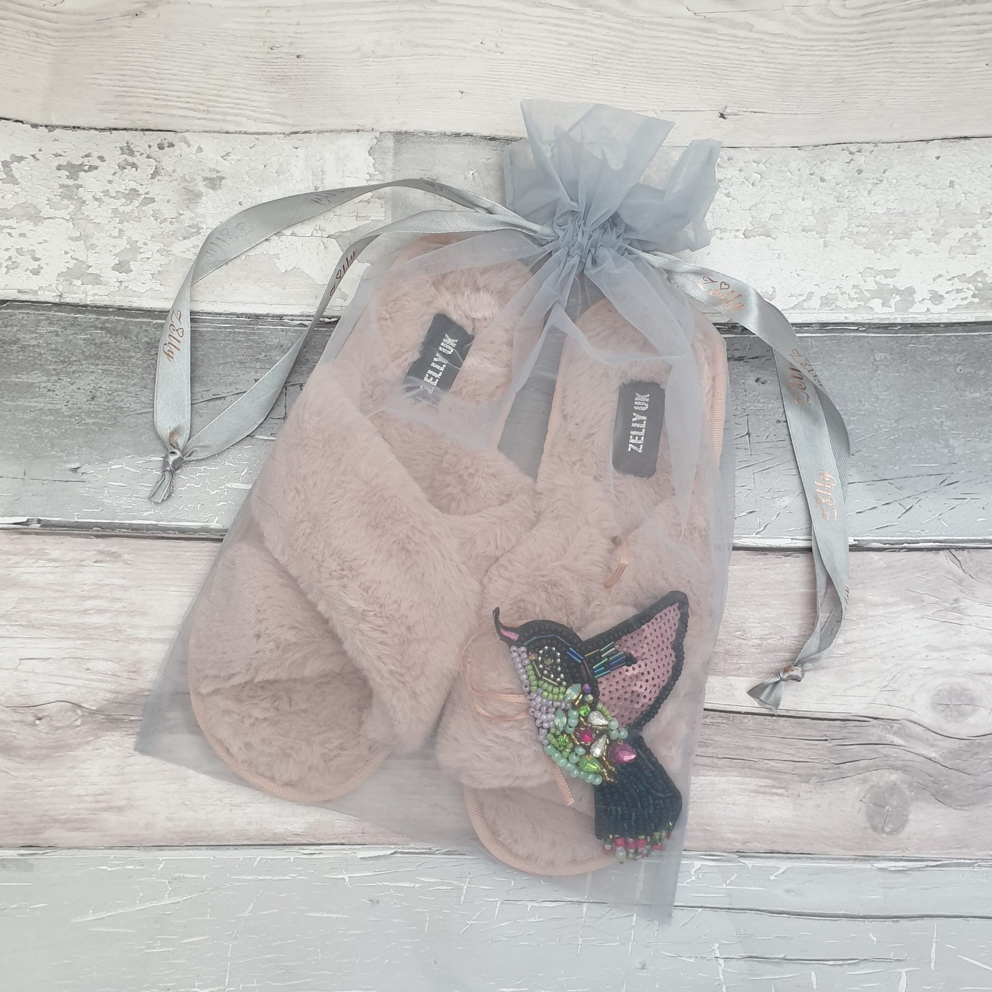 Fluffy pink slippers with a Pink and Green Hummingbird Brooch presented in a grey drawstring organza bag.