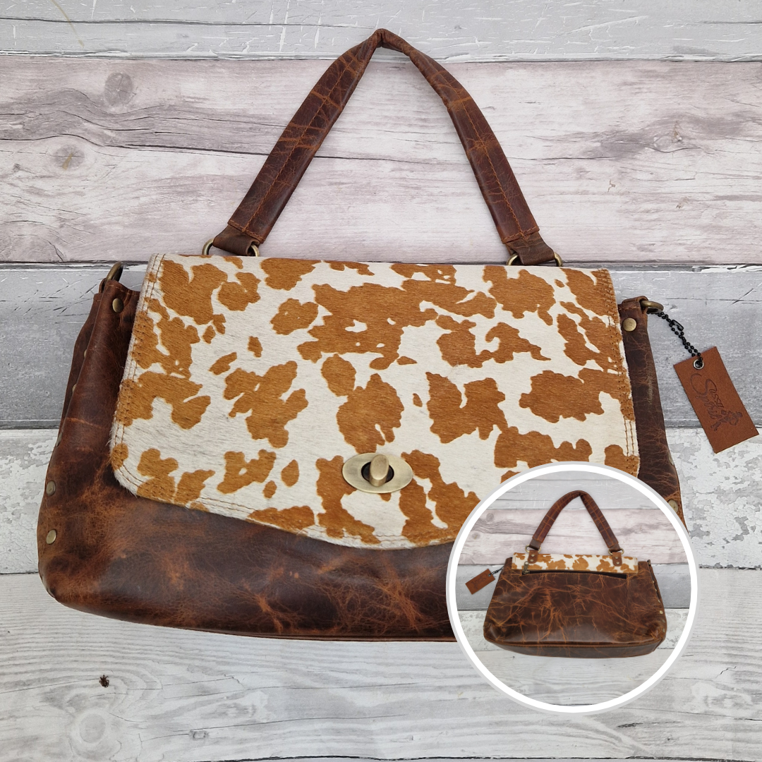 Brown leather and cow print fabric handbag on a wooden surface