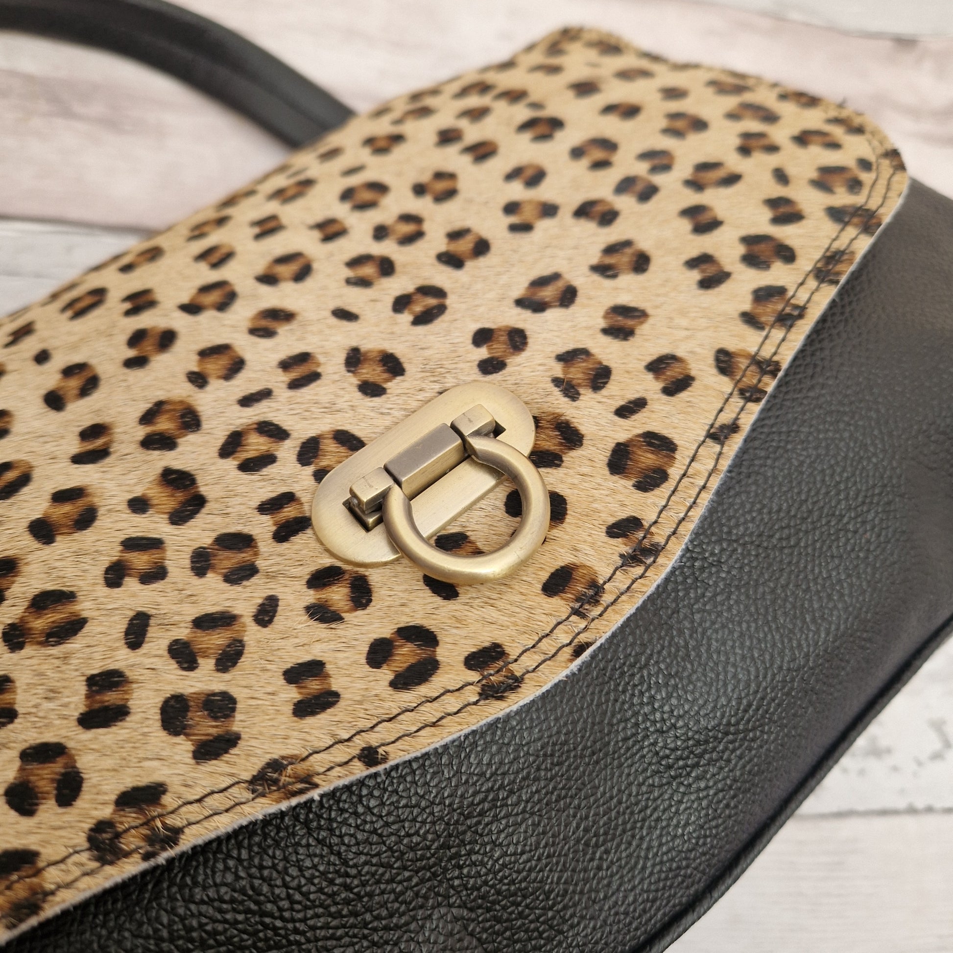 Leopard print handbag with a gold clasp on a light wooden surface