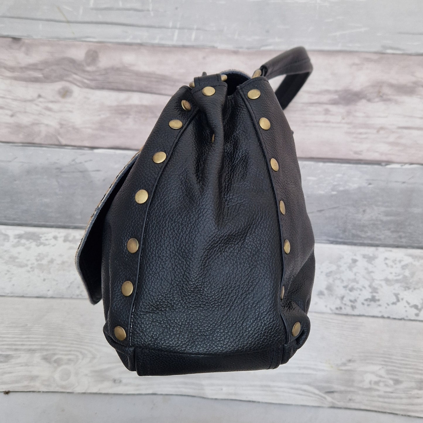 Black leather backpack with gold studs on a wooden surface