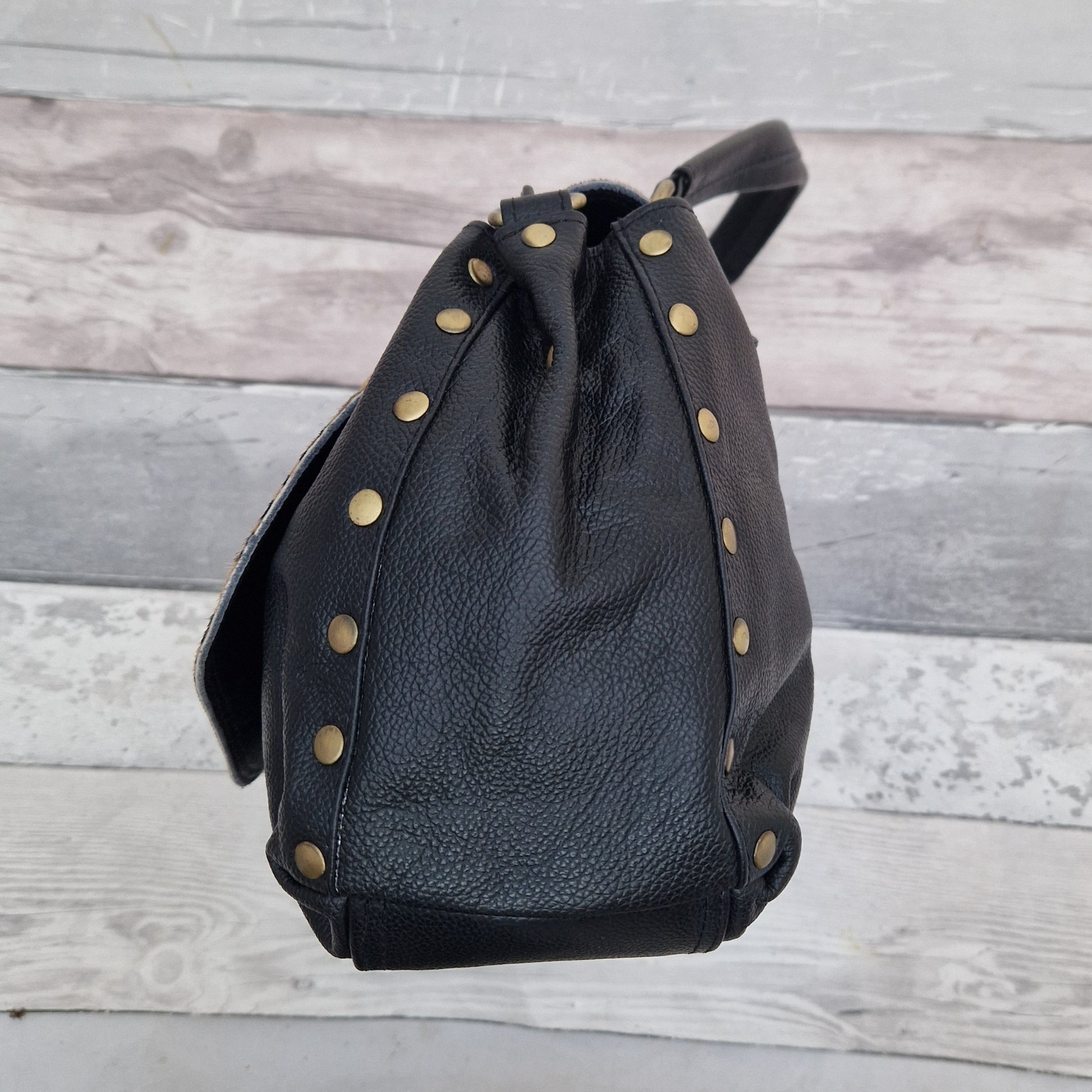 Black leather backpack with gold studs on a wooden surface