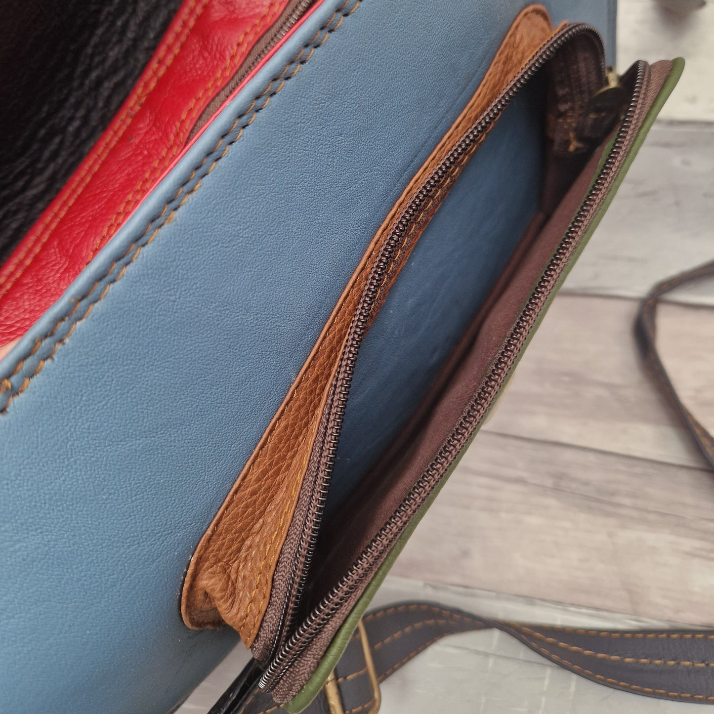 Close-up of a blue leather bag with brown zipper on a wooden surface
