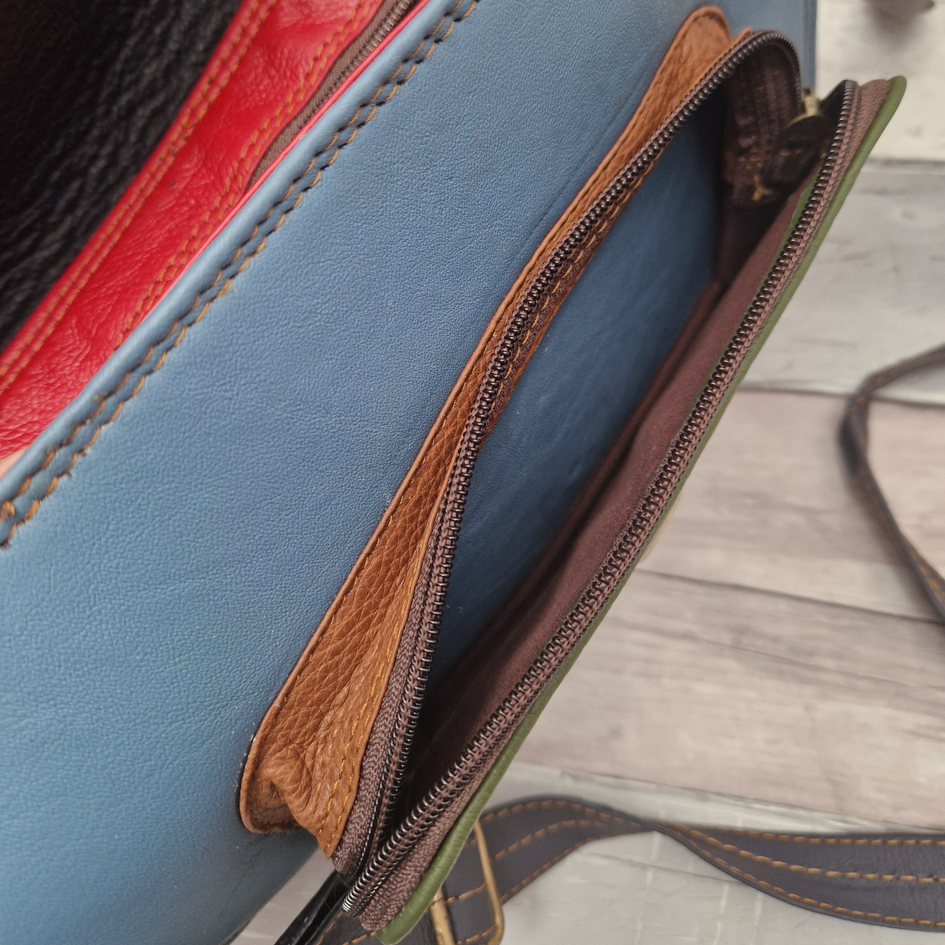 Close-up of a blue leather bag with brown zipper on a wooden surface