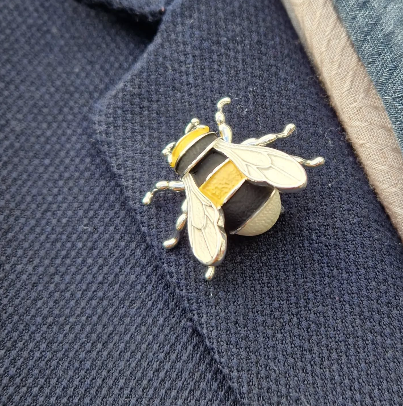 Silver bee-shaped brooch on a blue textured fabric background