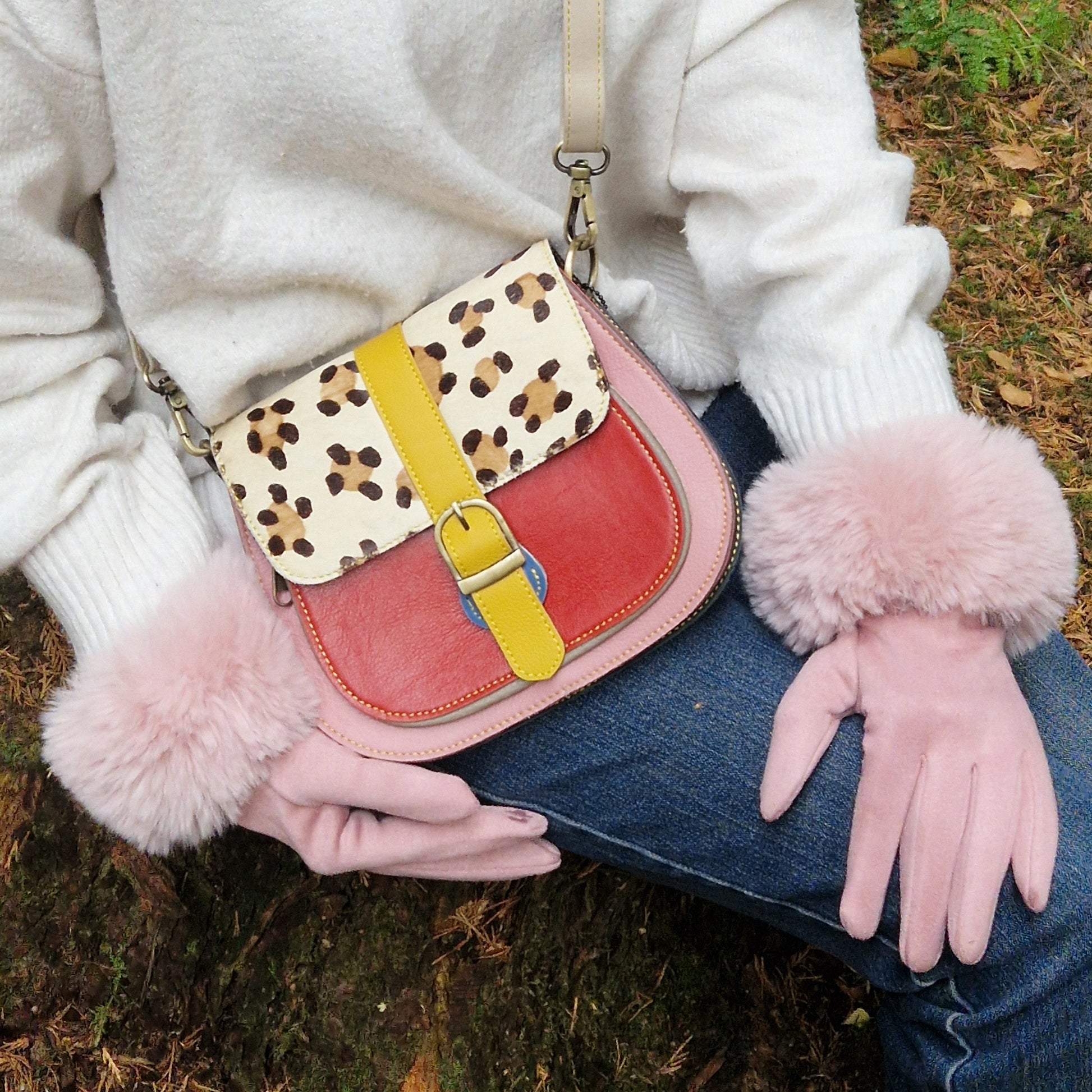 Person holding a colorful handbag with leopard print and pink accents, wearing a white sweater and blue jeans.