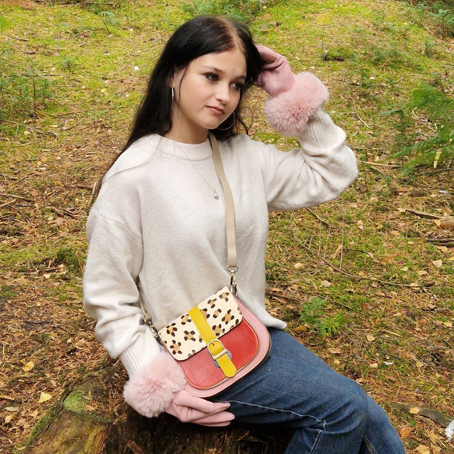 Woman holding a colorful handbag with a pink fluffy accessory in a forest setting