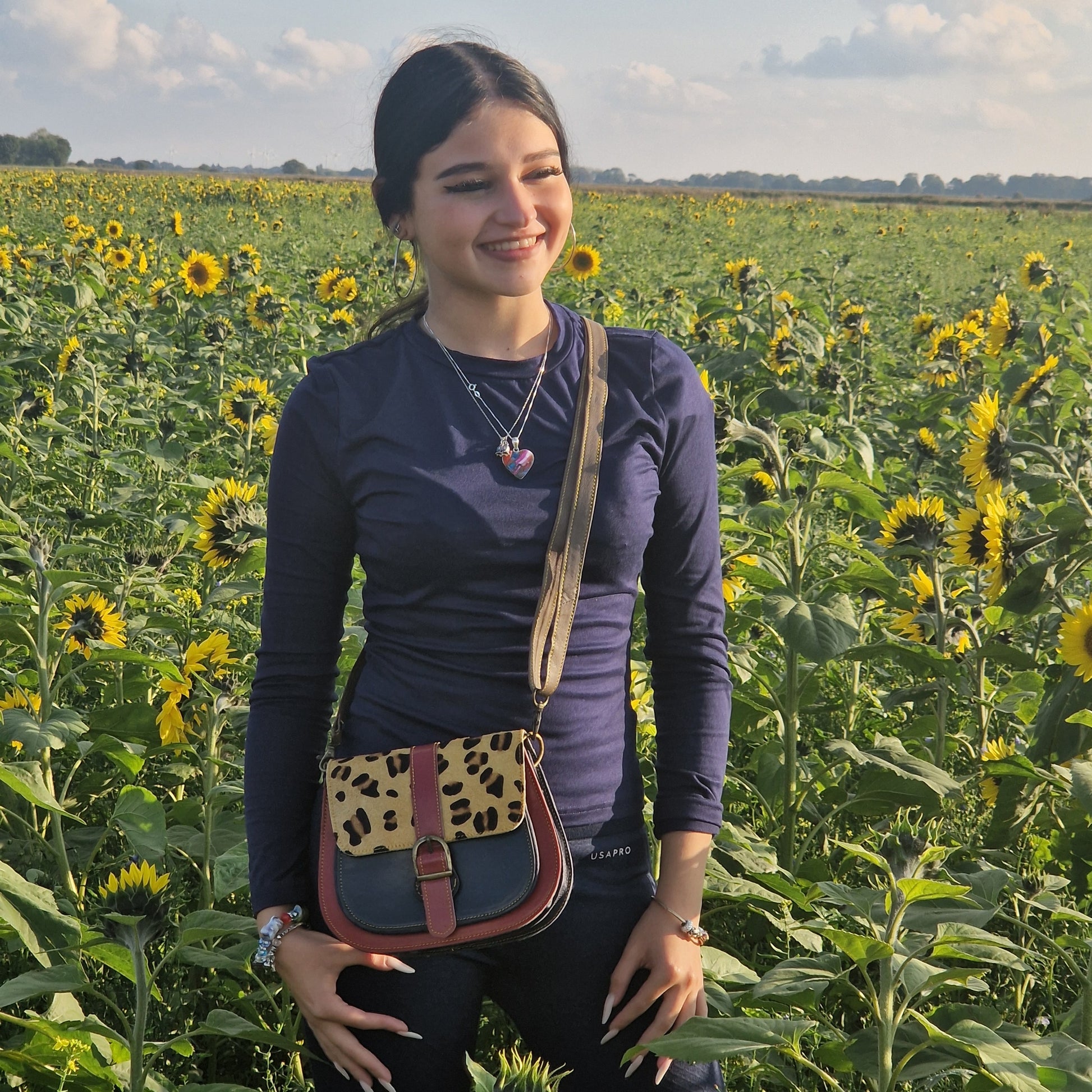 Woman standing in a sunflower field with a leopard print bag