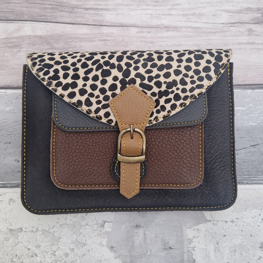 Mini satchel style crossbody bag made with in dark brown with contrasting coloured panels, a buckle closing tab and a textured panel of spot print.