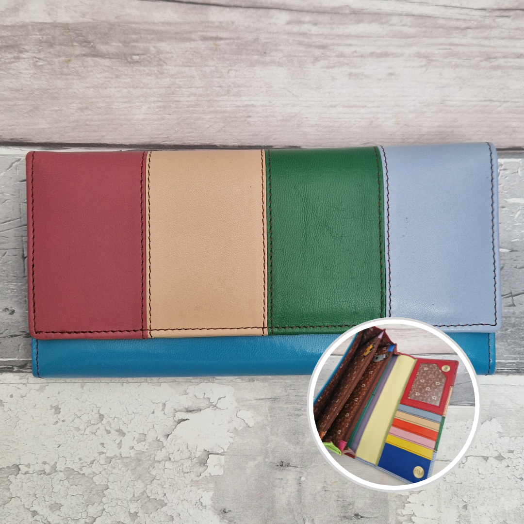 A long leather wallet with four vertical color panels in red, tan, green, and light blue, resting on a distressed gray wood surface. A circular inset in the lower right shows the wallet opened with cards inside.