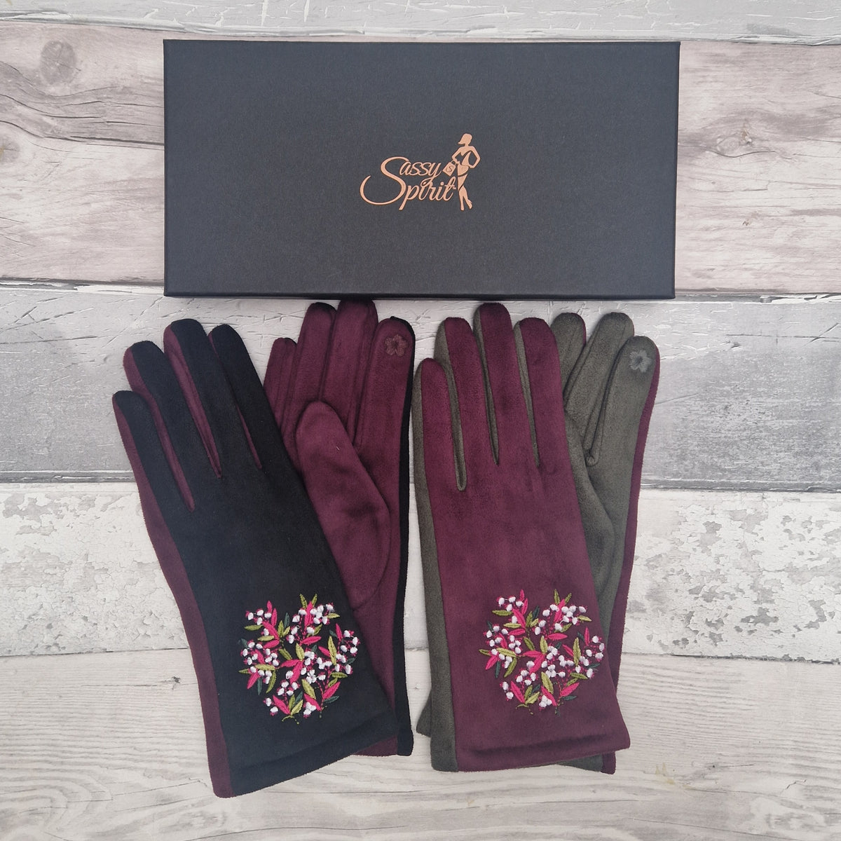 2 Pairs of gloves with floral embroidery on a gray wooden surface, accompanied by a black box labeled 'Sassy Spirit'.