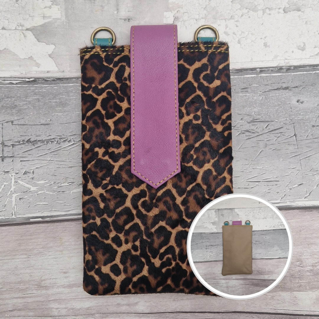 Leopard print phone pouch with a purple strap on a textured surface