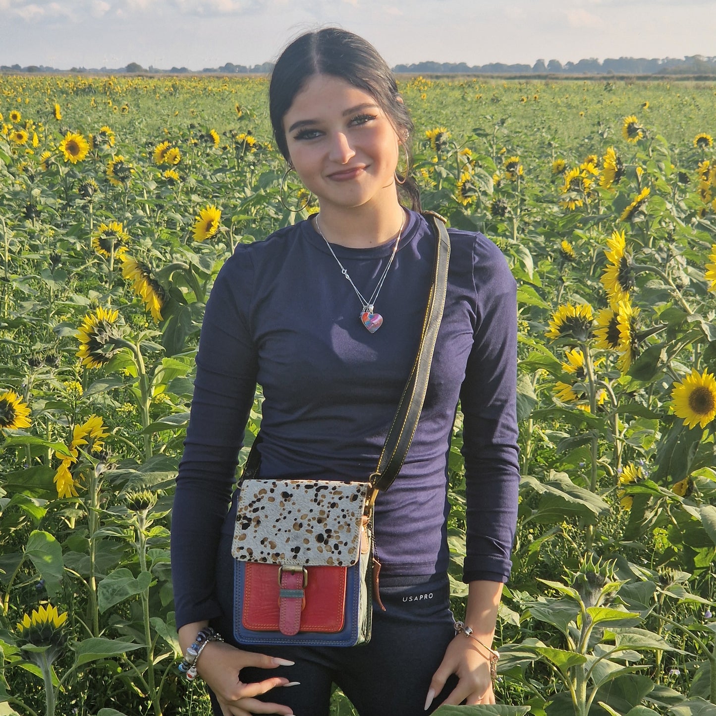 Woman standing in a sunflower field with a colorful bag