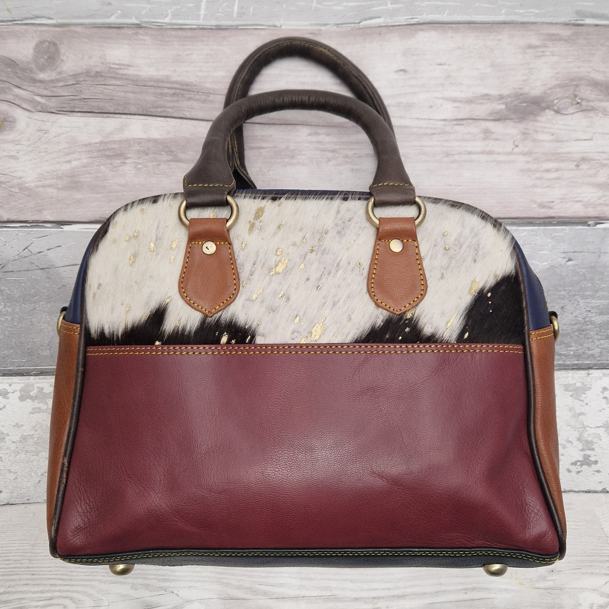 Bowling bag style handbag made from multi-coloured leather pieces. Textured panel of cow hide has been decorated with a striking gold metallic splatter.