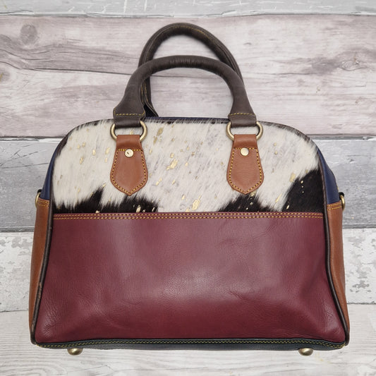 Bowling bag style handbag made from multi-coloured leather pieces. Textured panel of cow hide has been decorated with a striking gold metallic splatter.