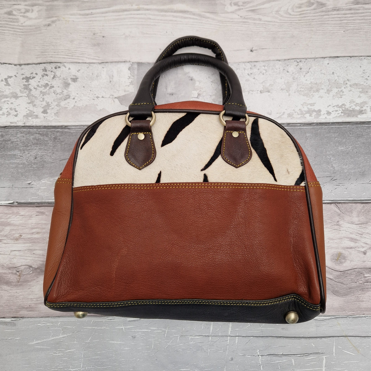 A leather crossbody bowling bag with carry handles, featuring a zebra animal print and brown panels