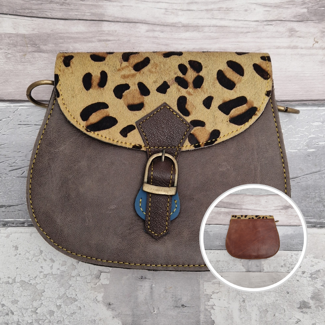 A saddle-style handbag with a taupe-brown suede body, a tan and black leopard-print flap, and brass-tone hardware, shown on a light weathered wood background with a circular inset showing the leopard-print edge detail.