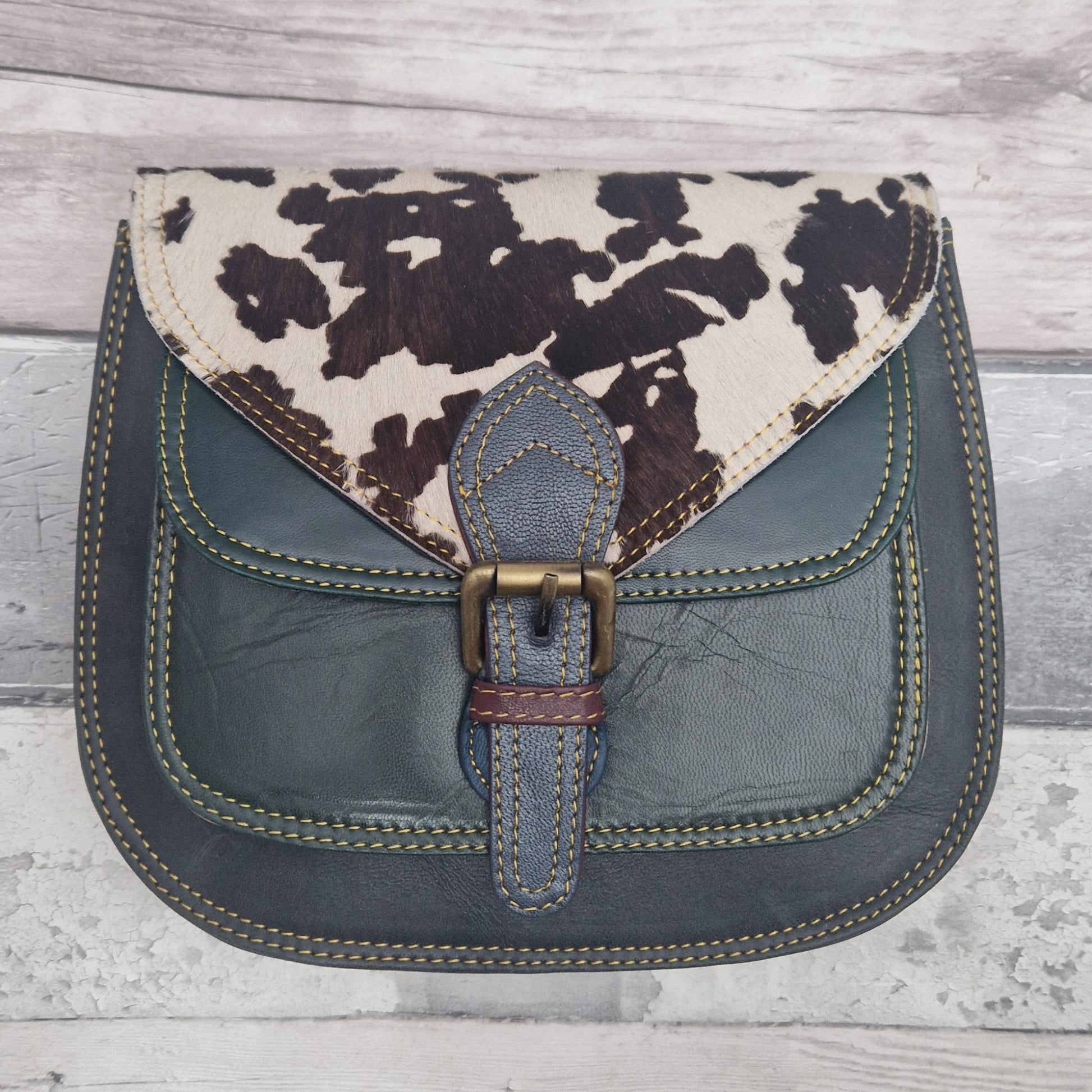 Saddlebag style Handbag with cow print top section and blue body on a wooden surface