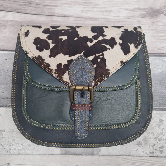 Saddlebag style Handbag with cow print top section and blue body on a wooden surface