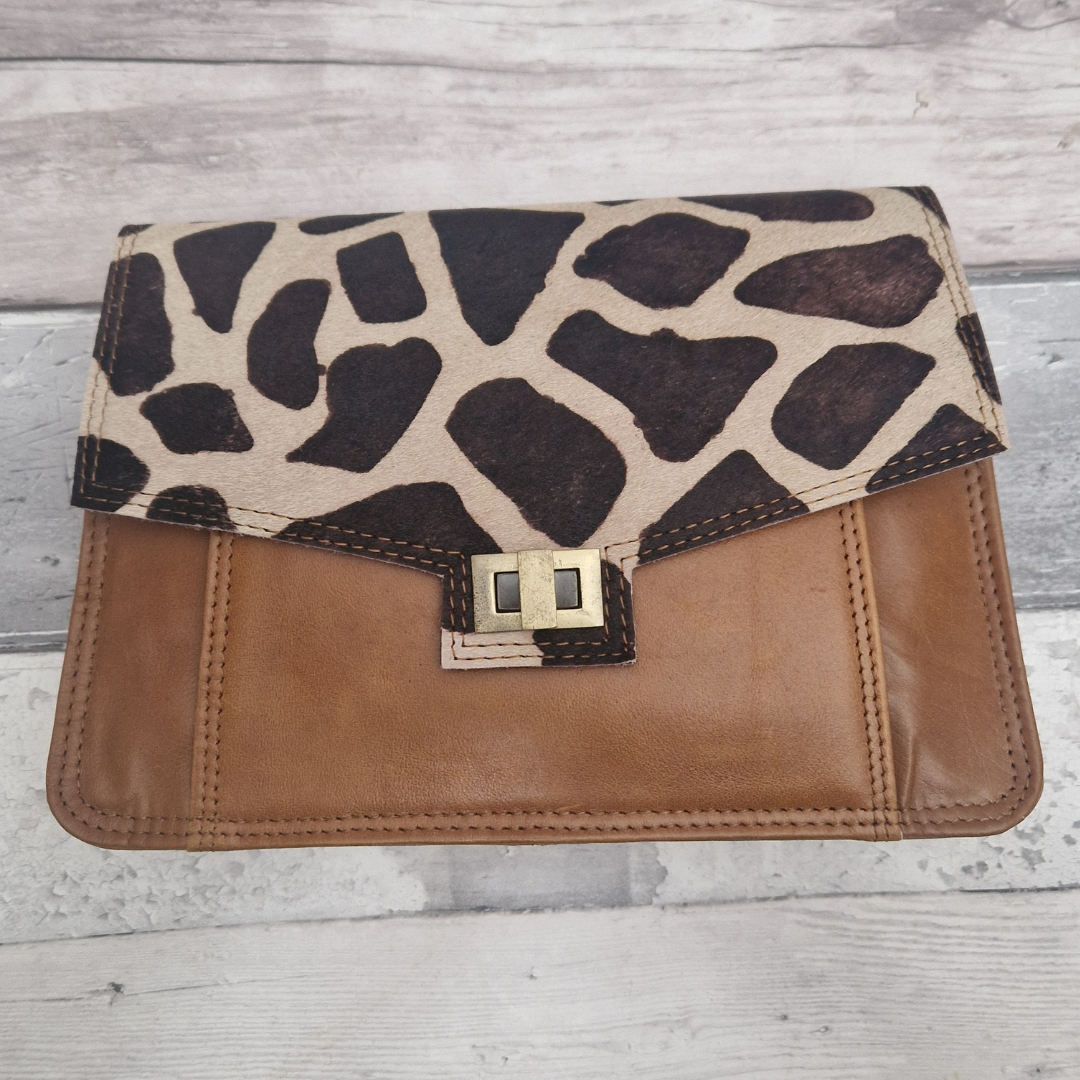 Giraffe print and tan brown leather clutch bag on a wooden surface