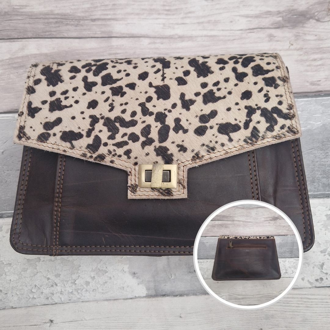 Cow print clutch bag on a wooden surface with a close-up inset showing the reverse side.