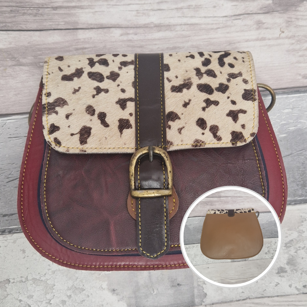 All leather saddlebag style ladies bag in 2 tones of burgundy with a textured panel of cow print. Brass buckle closer.