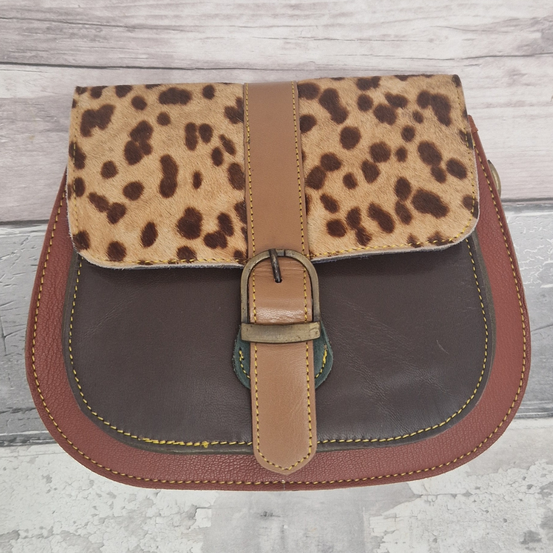 All leather saddlebag style ladies bag in 2 tones of brown and with a textured panel of spot print. Brass buckle closer.