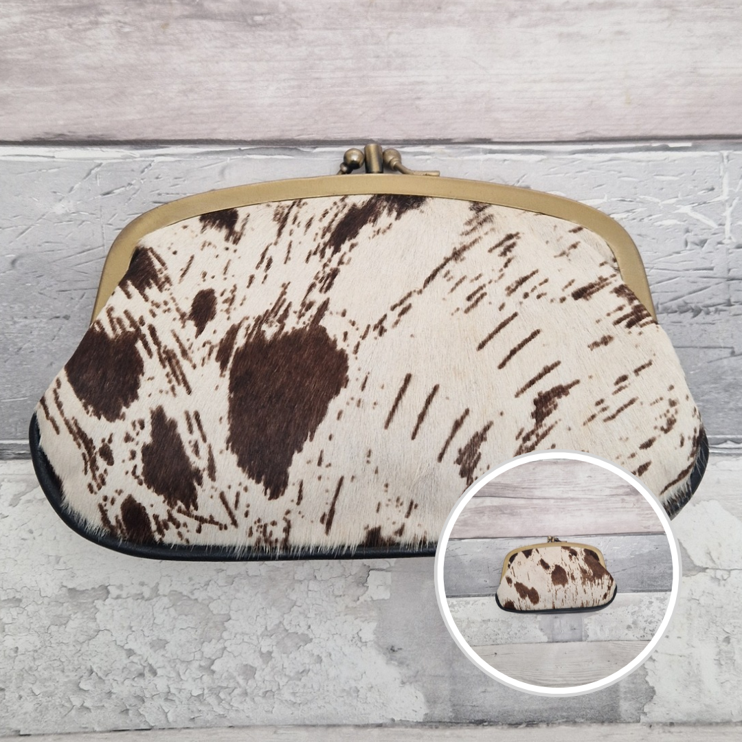 A small handbag with a brown and cream cowhide pattern, a gold-tone metal frame, and a kiss-lock clasp, displayed on a light gray wood background with a circular inset showing the bag from the front.
