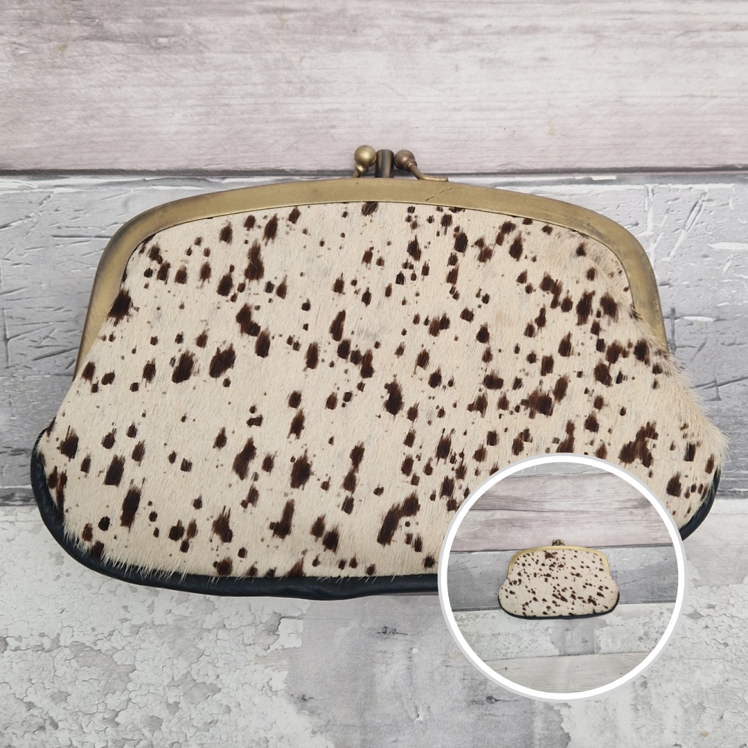 A vintage-style kiss-lock clutch bag made of cream-colored cowhide with dark brown spots, featuring a brass-tone metal frame. A circular inset in the bottom right shows a close-up of the patterned hide.