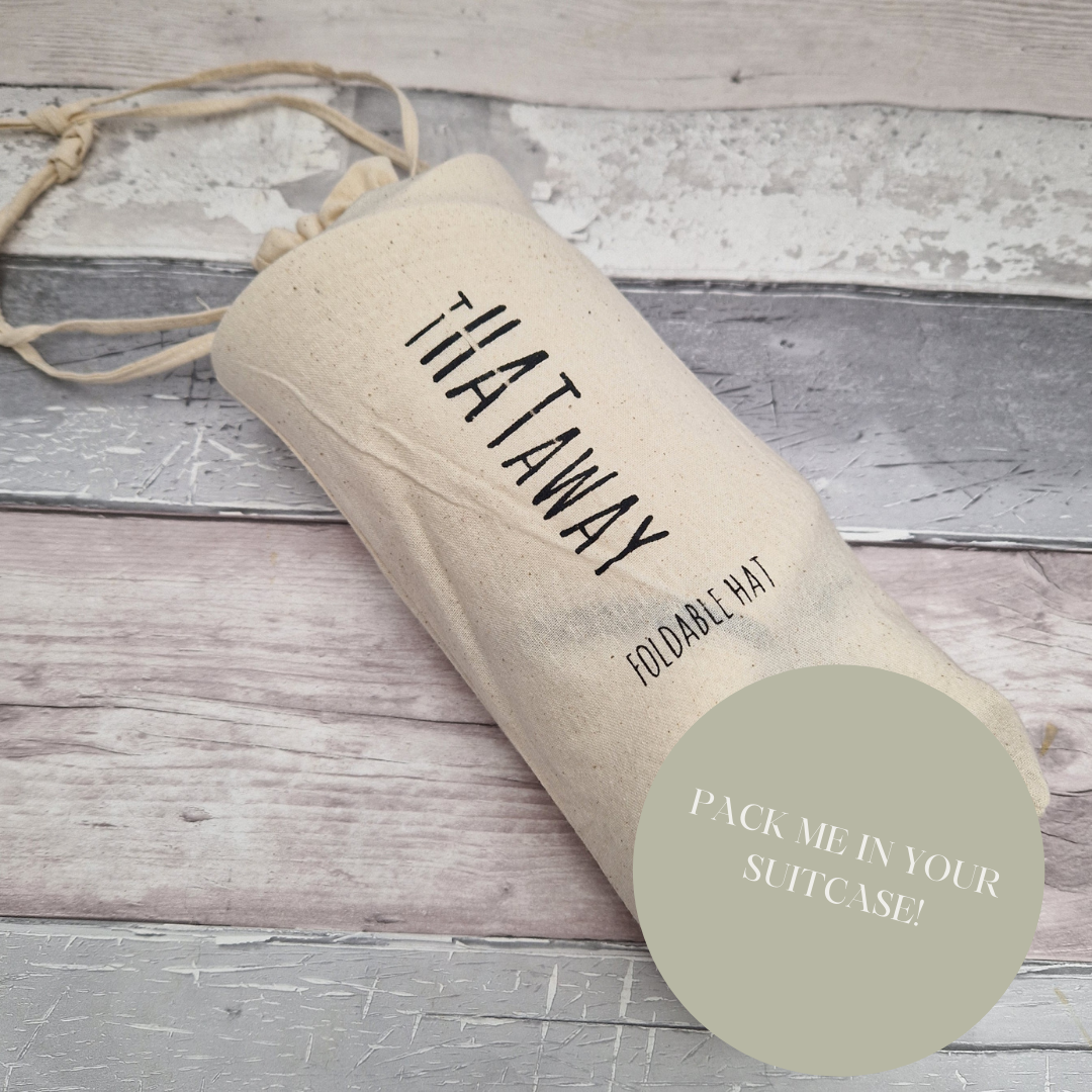 A rolled up hat inside a cream cotton bag with a banner saying "pack me in your suitcase".