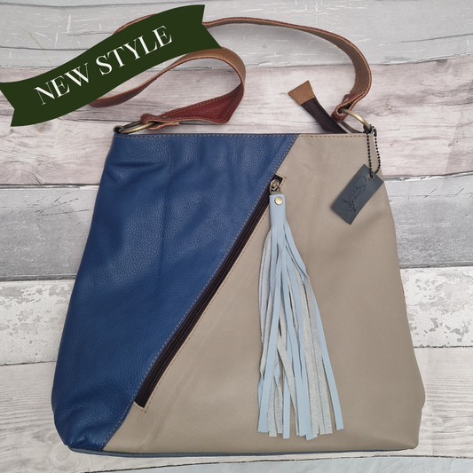 Soft leather tote bag with single long handled strap. Blue and stone coloured front split diagonally with a zip pocket finished with a pale blue leather tassel.