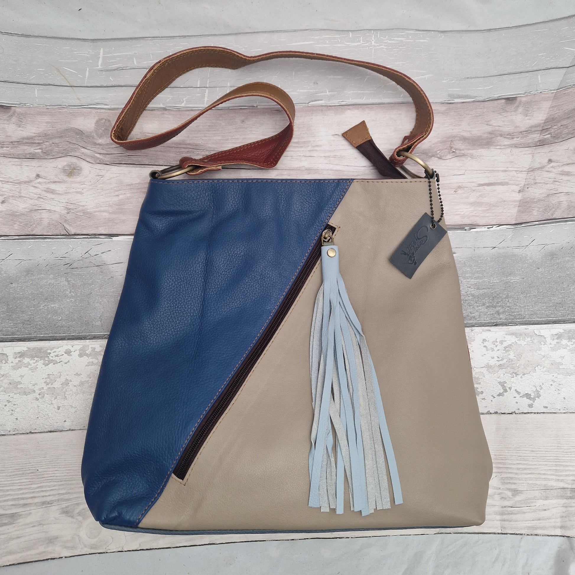 Leather tote bag with 2 coloured panels of stone and blue separated by a zip pocket with a tassel pull.