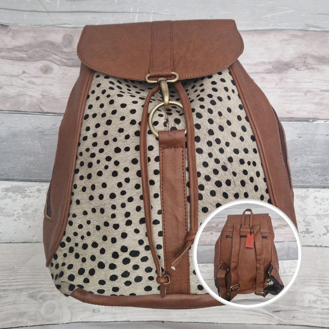 Backpack with brown leather straps and a polka dot pattern on a wooden surface.