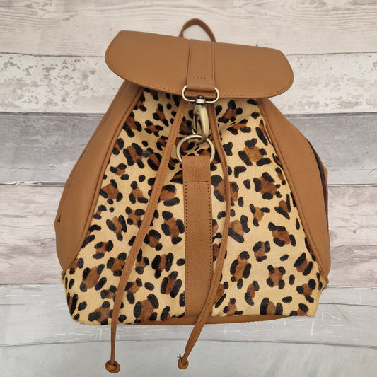 Leopard print backpack with brown leather accents on a wooden background