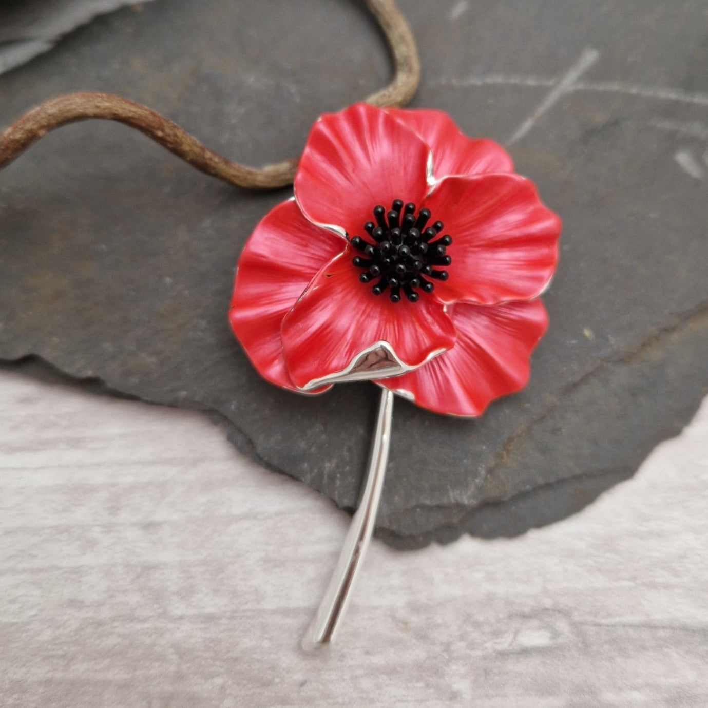 Striking red poppy brooch with black centred stamen and a long silver stem.