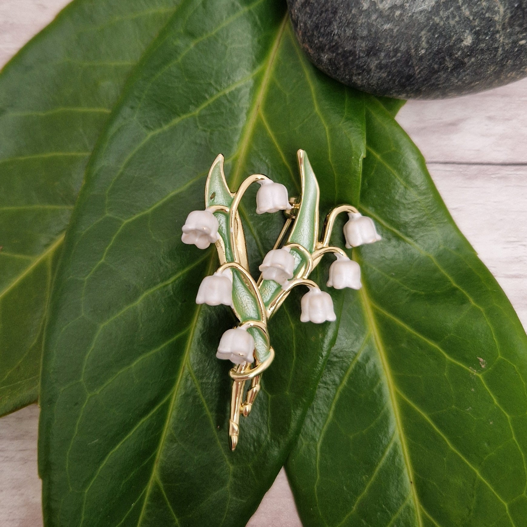 Photo of a spray of Lily of the Valley white flowers and green leaves formed as a ladies brooch with a gold stem