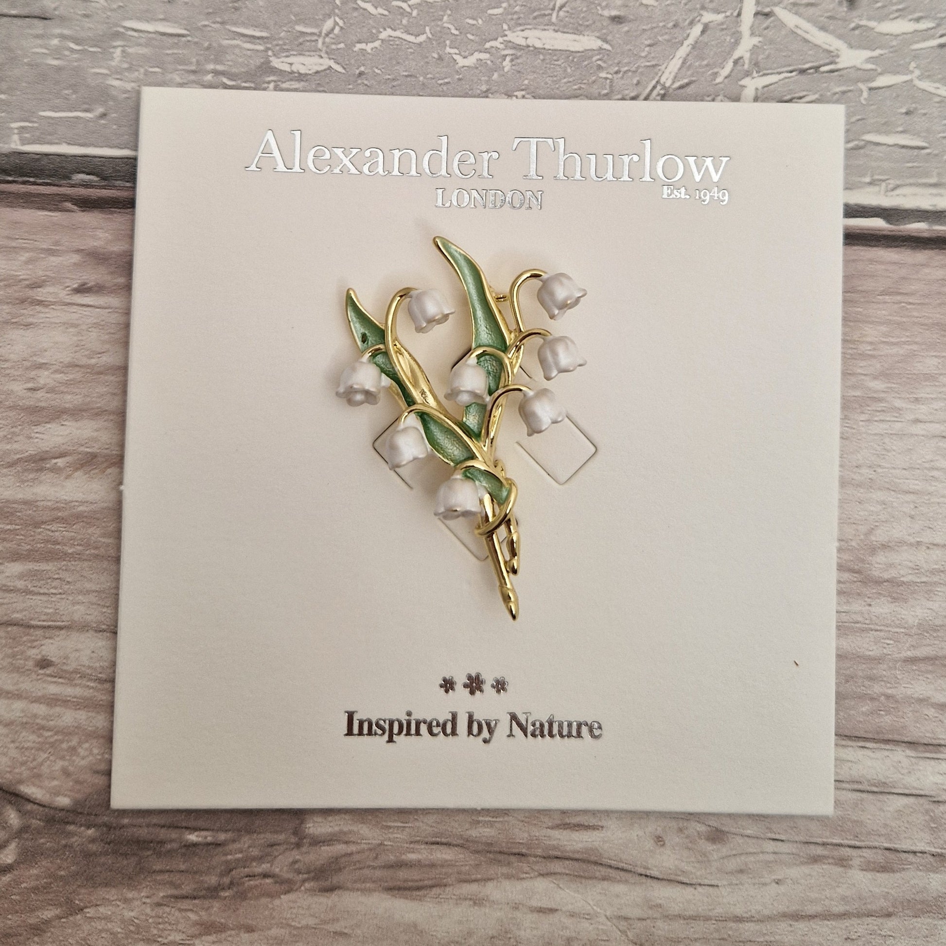 Photo of a spray of Lily of the Valley white flowers and green leaves formed as a ladies brooch with a gold stem on a display card.