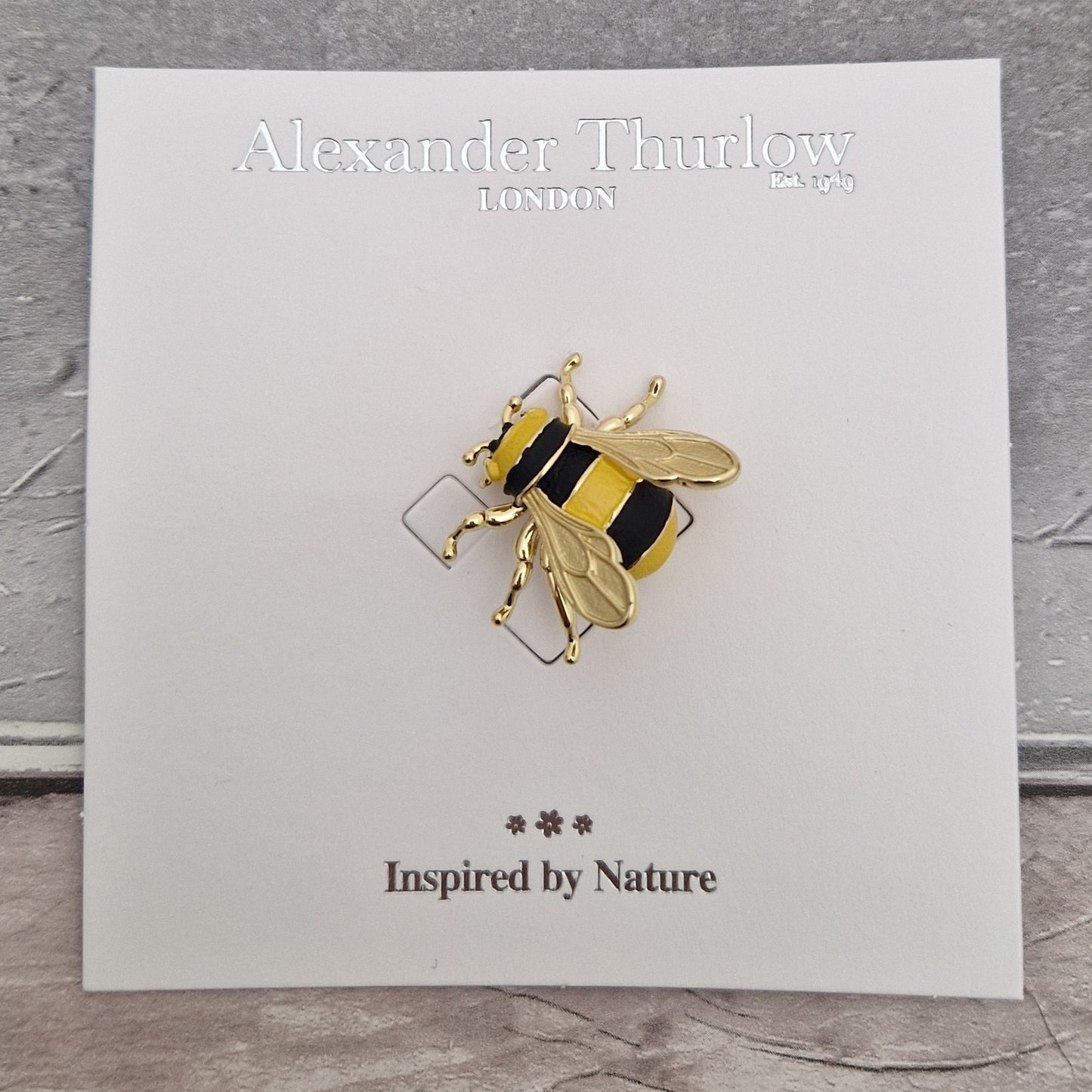 Gold and black bee-shaped brooch on a card with 'Alexander Thurlow London' branding.