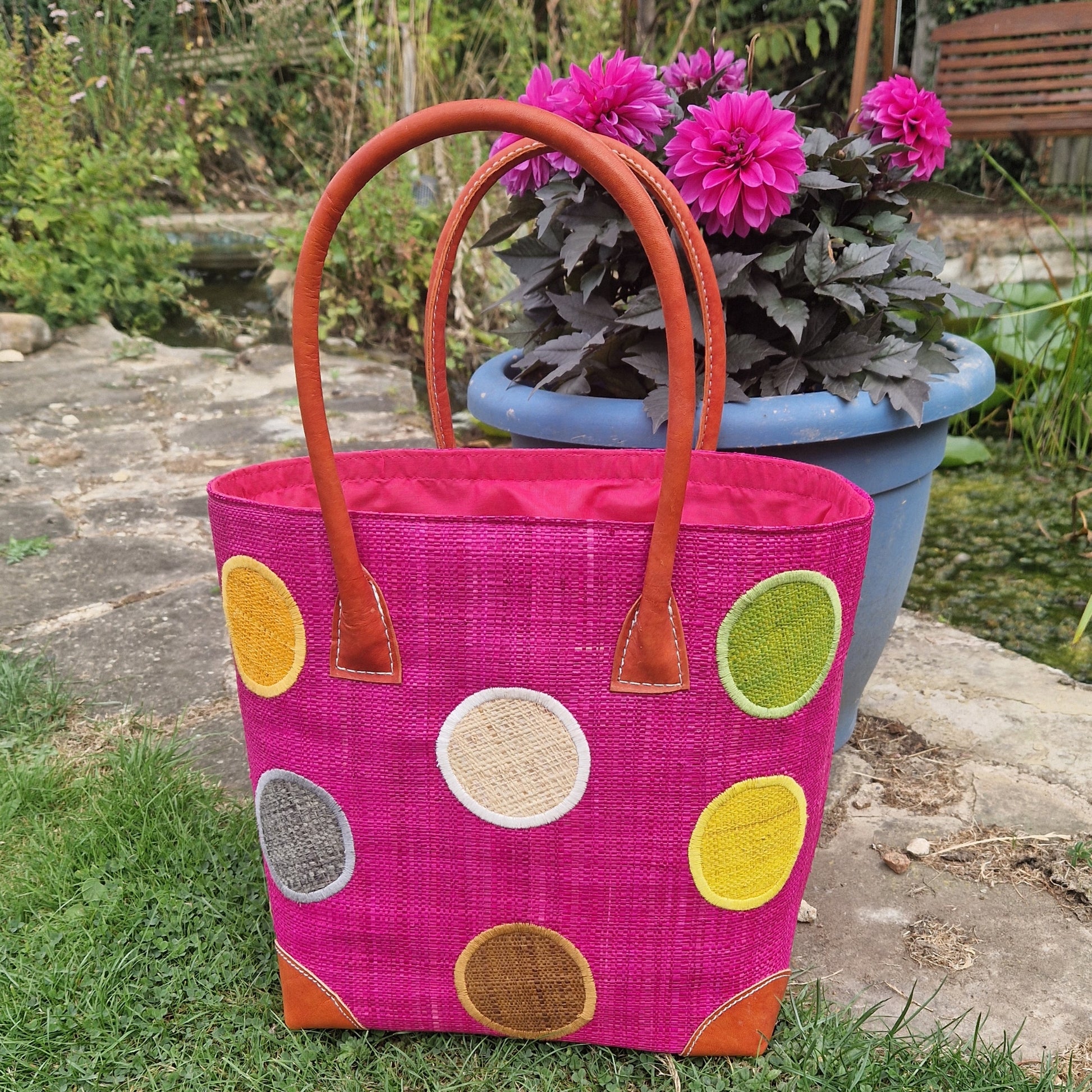 Pink Raffia basket with leather handles decorated with multi coloured spots.