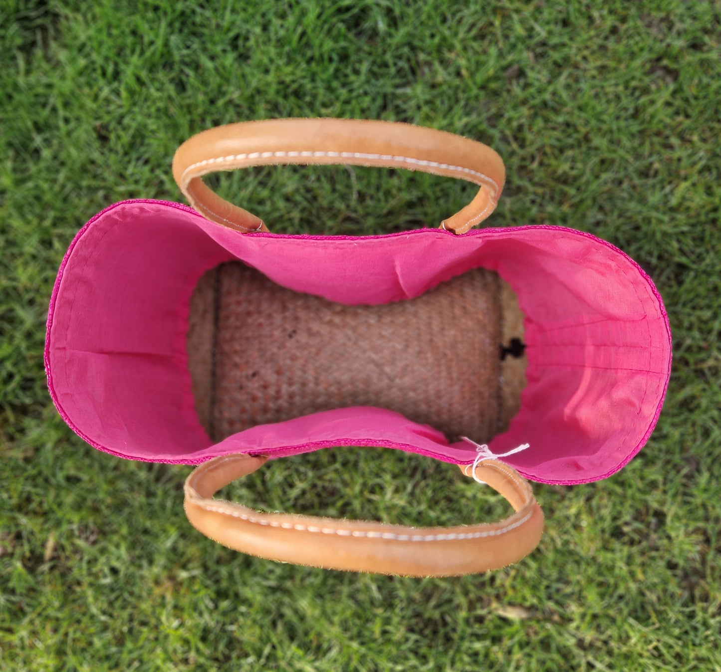Top down view of the inside of a pink raffia basket with leather handles.