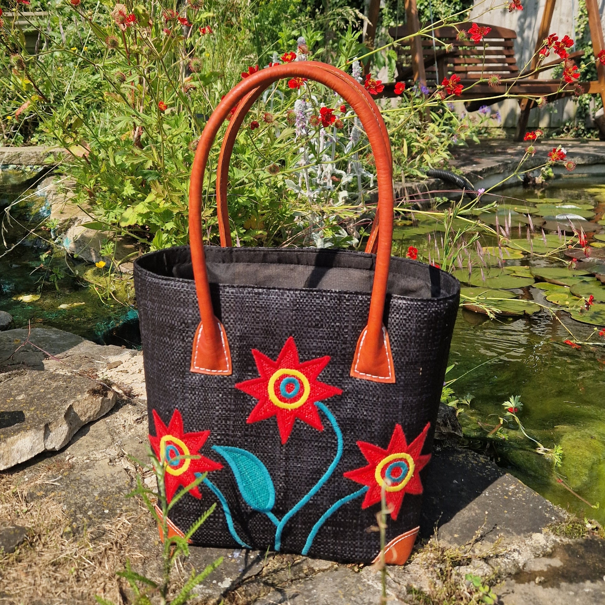 Black Raffia Basket with leather handles. Decorated with 3 stems of Red sunflowers.