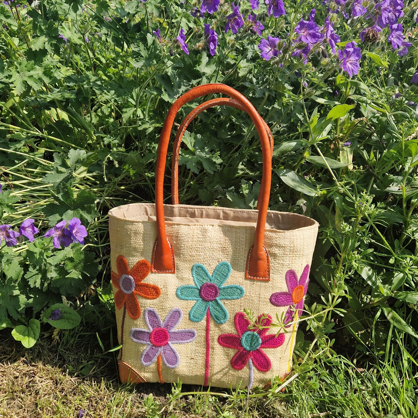 Natural Raffia basket with leather handles. Decorated with an image of 5 multi-coloured flower stems.