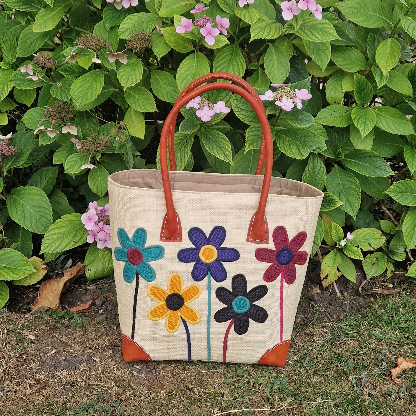 Natural Raffia basket with leather handles. Decorated with an image of 5 multi-coloured flower stems.