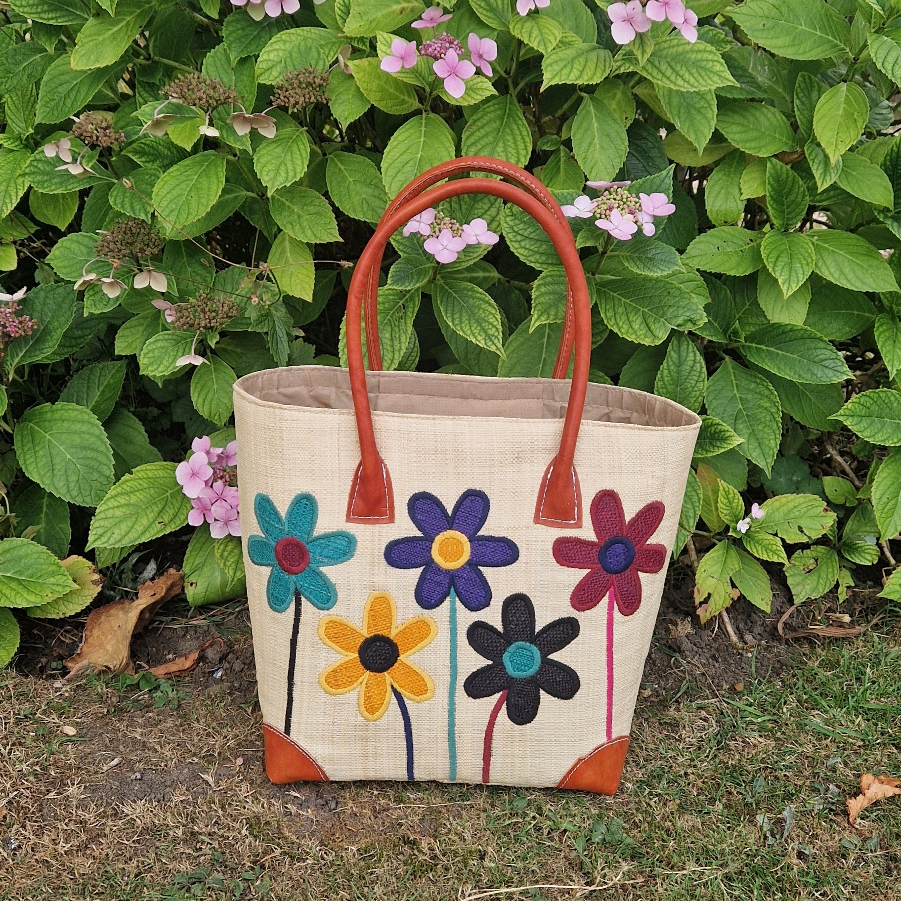 Natural Raffia basket with leather handles. Decorated with an image of 5 multi-coloured flower stems.