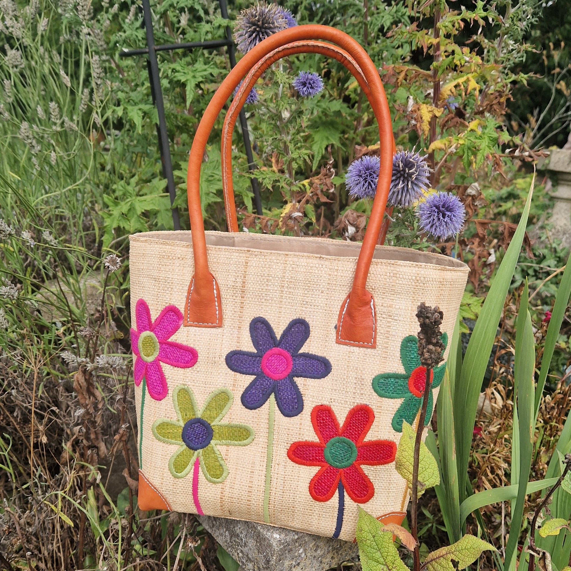 Natural Raffia basket with leather handles. Decorated with an image of 5 multi-coloured flower stems.