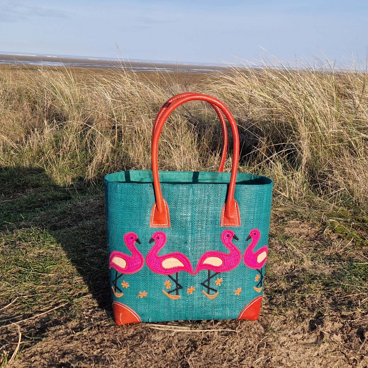Turquoise coloured raffia basket decorated with pink flamingos.