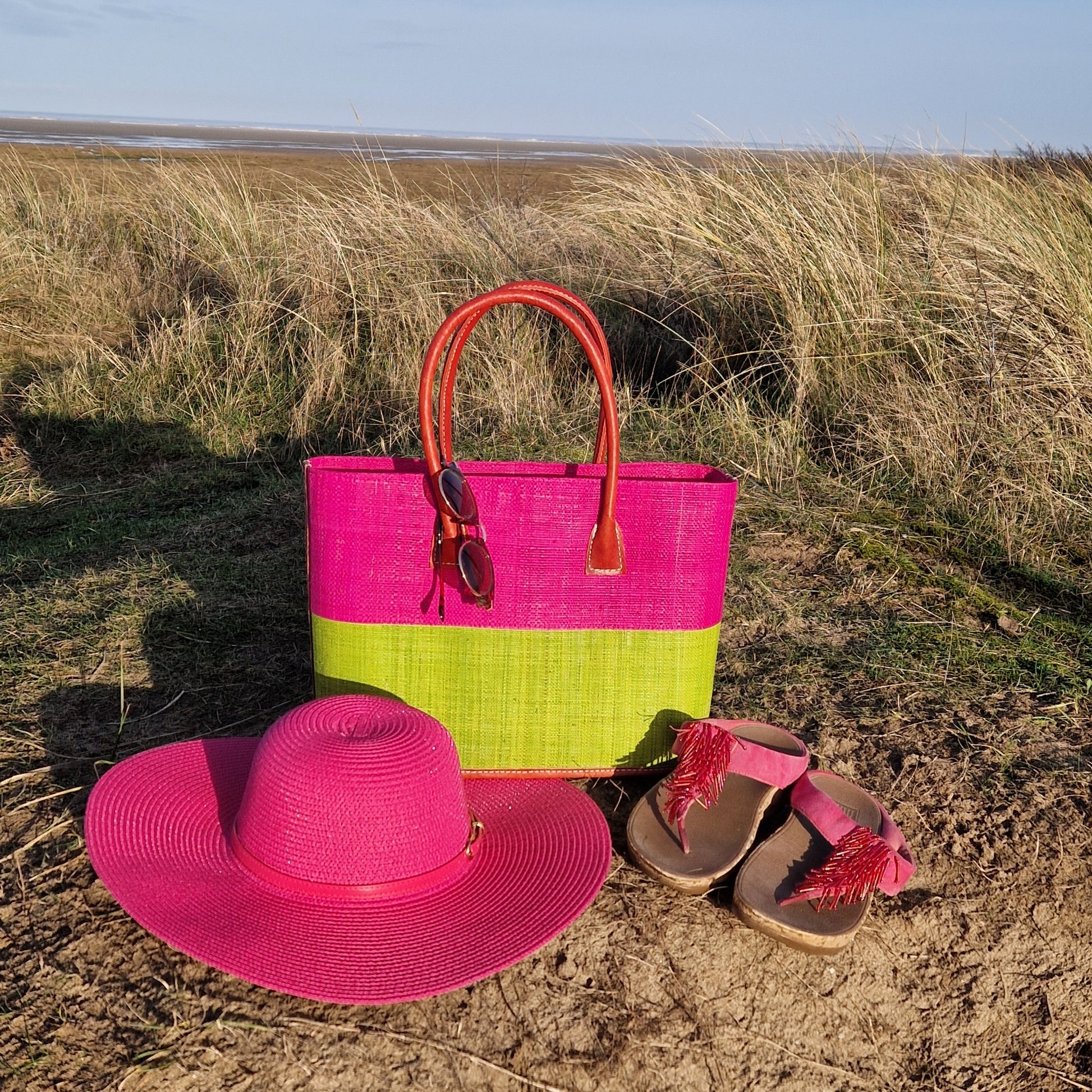 Raffia basket with leather handles in panels of hot pink and lime. Pictured with a matching pink wide brimmed hat.