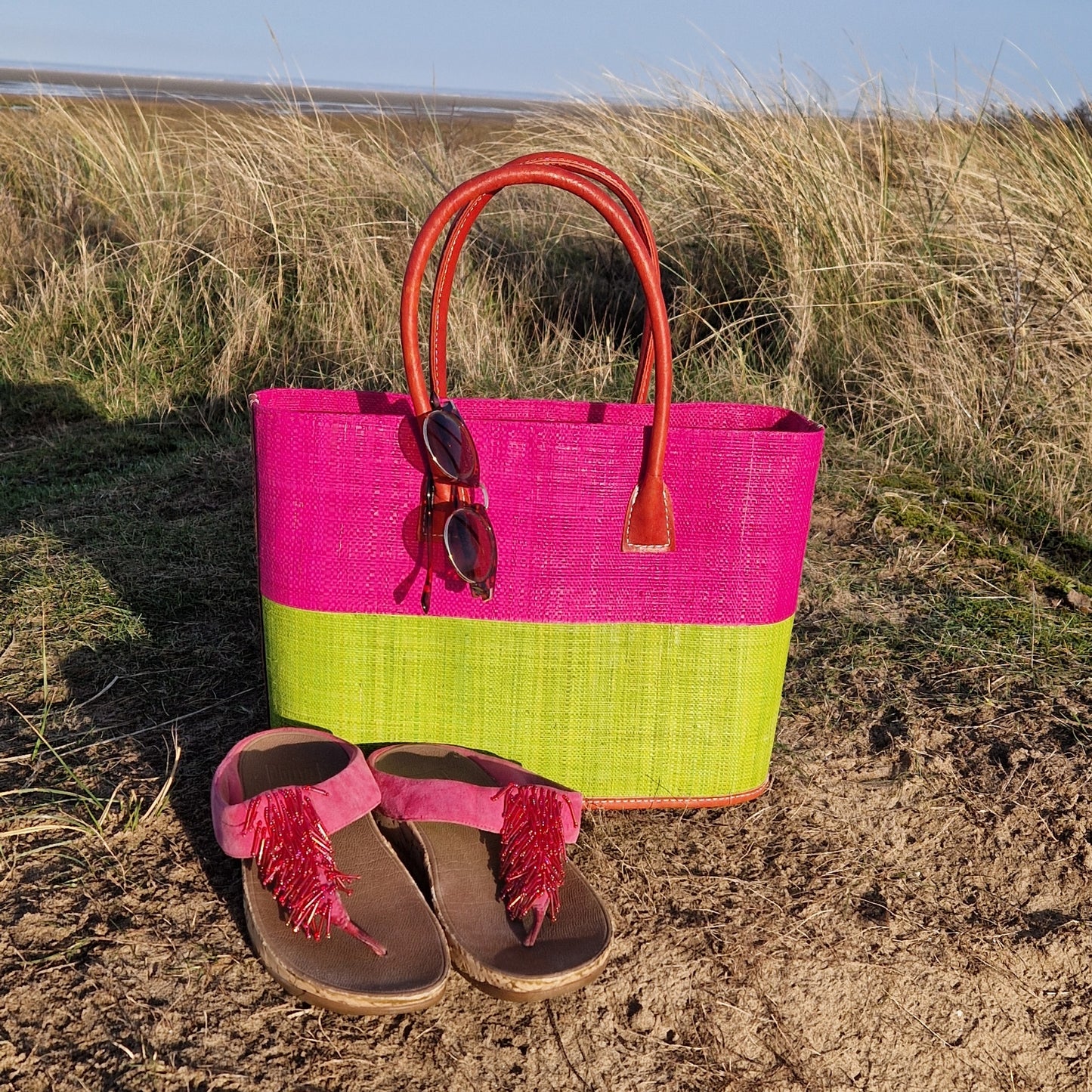 Raffia basket with leather handles in panels of hot pink and lime.