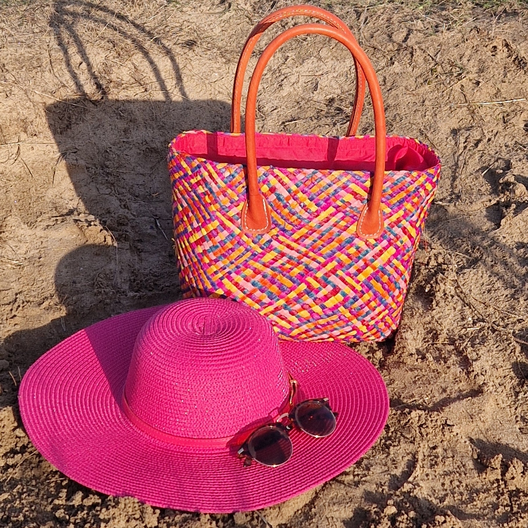 Raffia basket with a multicoloured patchwork pattern and matching pink wide brimmed hat.